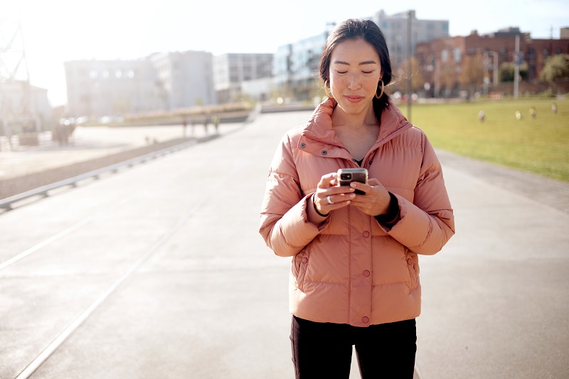 Woman in jacket outdoors on urban walkway looking at cellphone