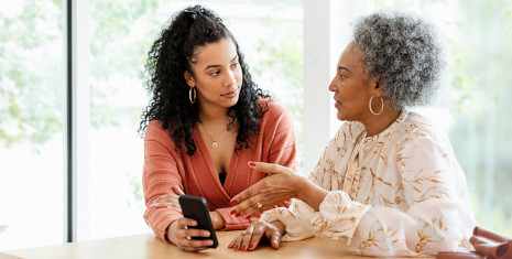 Two women at a table talking and holding a mobile phone.