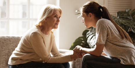 Mother and daughter sitting across from each other holding hands