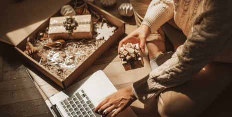 Woman seated on the floor with a gift box in hand and a laptop