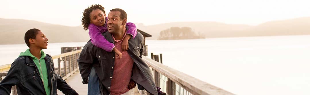 Father carrying daughter on his back with son walking next to them on a bridge