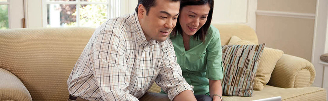 Man and woman sitting on a couch looking at a laptop