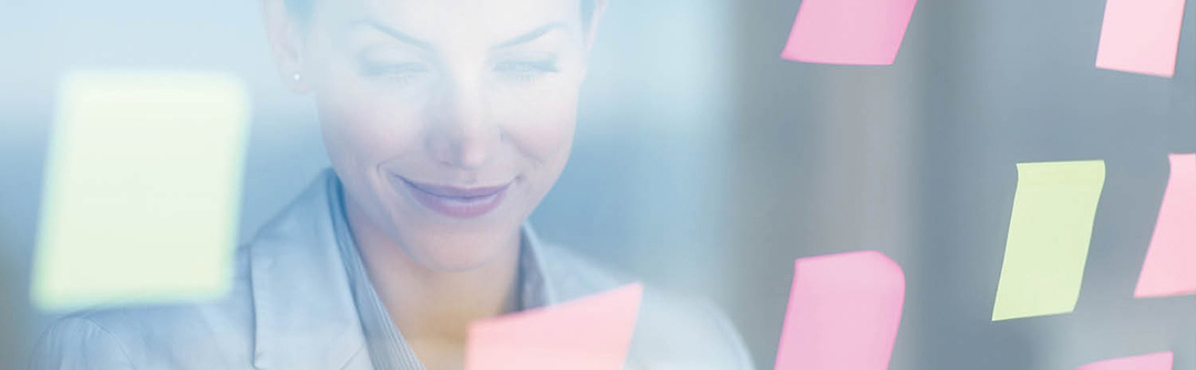 Woman looking and smiling at a glass wall with colorful sticky notes on it