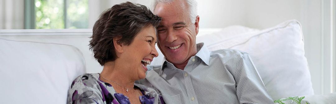 Older couple sitting close together on the couch laughing