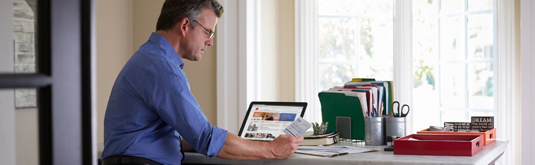 a man standing at a table looking at a piece of paper he's holding