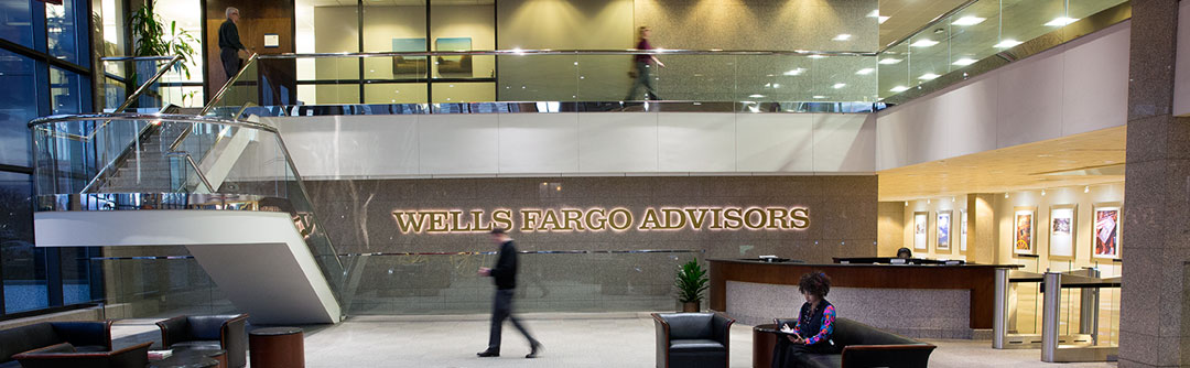 People walking around the lobby of a Wells Fargo Advisors office; staircase on the left side and a reception desk on the right