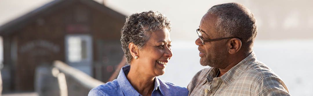 A couple standing outside in front of a house looking at each other and smiling