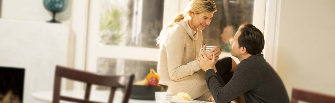 Woman sitting on table smiling with man sitting in chair. Woman is holding a coffee mug