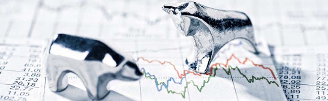 Silver figurines of a bear and bull standing on top of a market chart