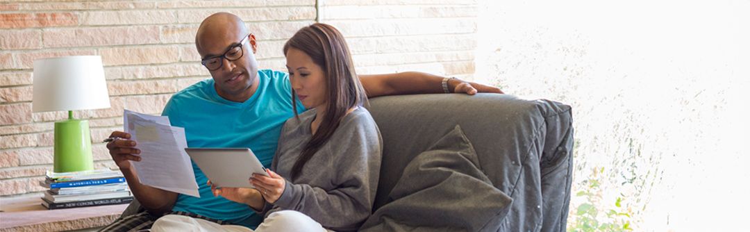 Man and woman sitting close together in a sofa chair looking over documents in their hands