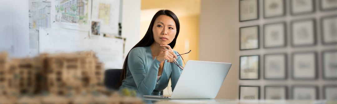 Woman in office holding glasses in front of laptop