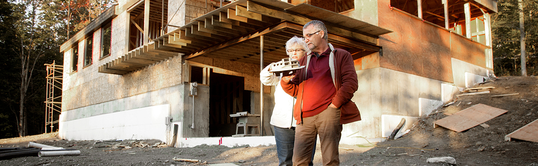 man and woman looking at a model house in front of a house under construction
