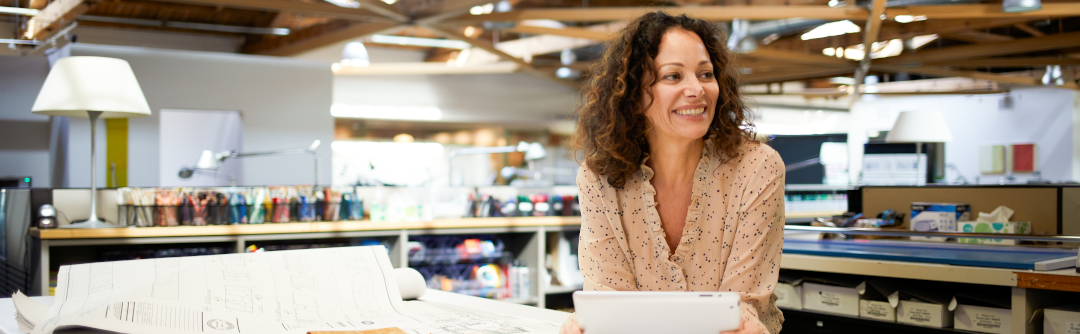 Woman in an office leaning on a drafting table and smiling