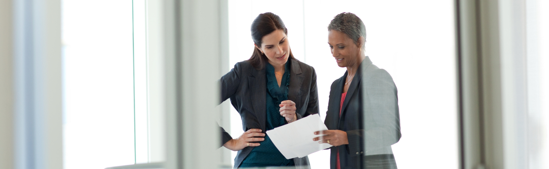 Two women standing in an office looking over paper documents and discussing them
