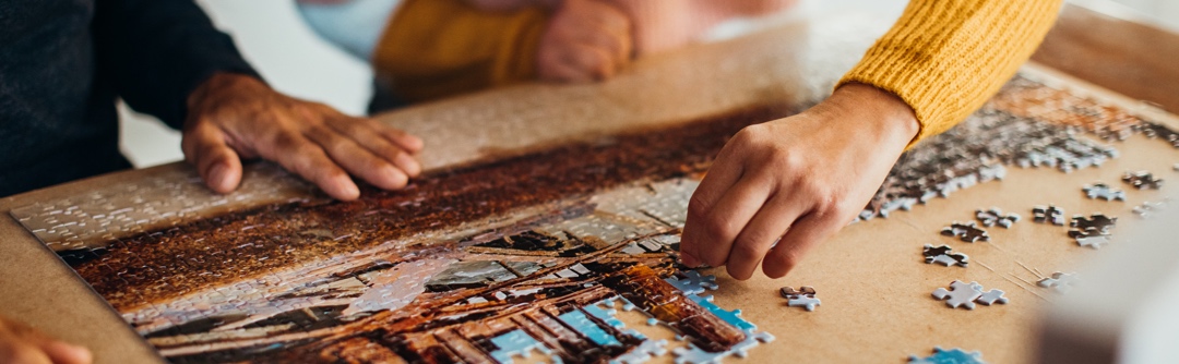 Closeup view of two people putting together a jigsaw puzzle on a table