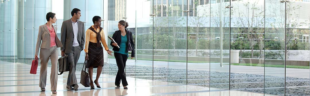 Three women and one man walking and talking down a hallway in an office building with large walls