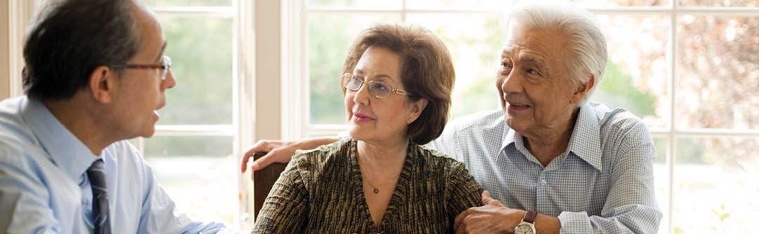 Man and woman sitting at a table in front of large windows speaking with their financial advisor