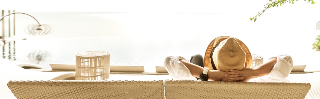 Person wearing a straw fedora sitting on an outdoor couch looking at horizon