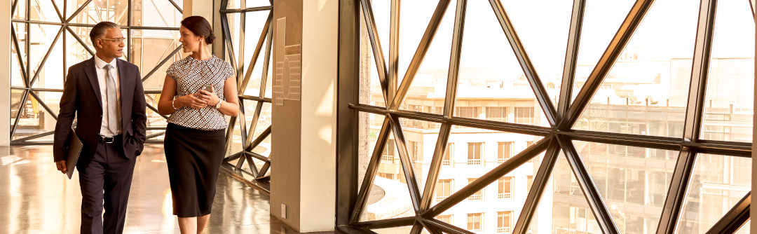 Business man and woman walking and talking in an industrial building with big windows