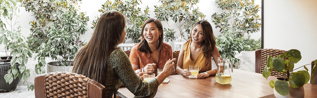 3 women sitting around a table on a patio talking