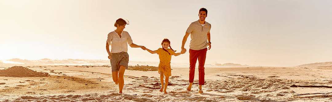 Mother and father holding child's hand while walking on the beach