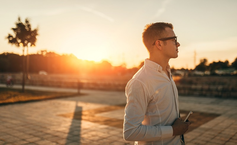 A man holding his phone as the sun sets in the background