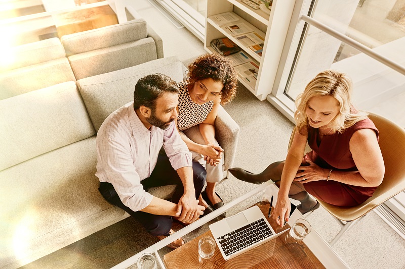 A couple sitting down with an advisor, reviewing plans on a laptop