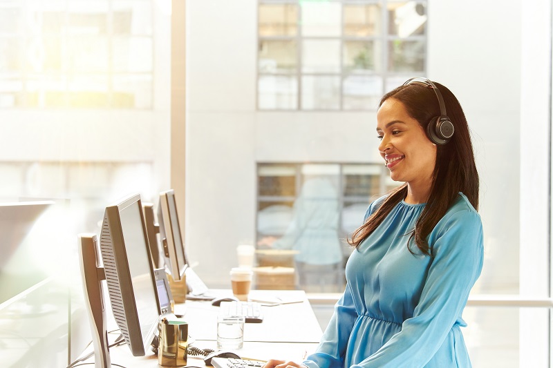 Woman with headset standing in front of table with monitors.