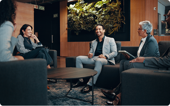 Five people seated in a modern lounge area having a group conversation around a coffee table.