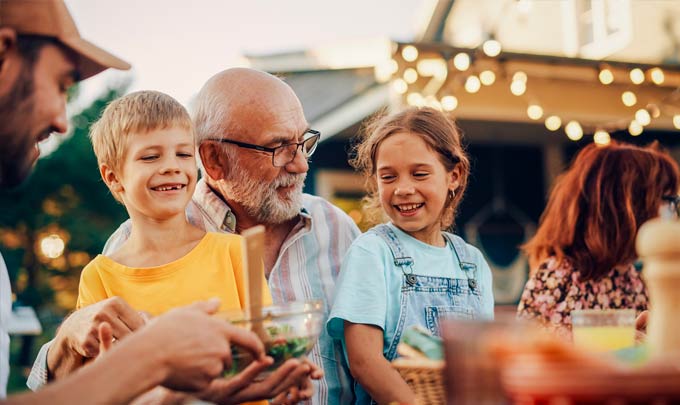 Two children and an older adult gathered at an outdoor table, with two additional adults nearby.