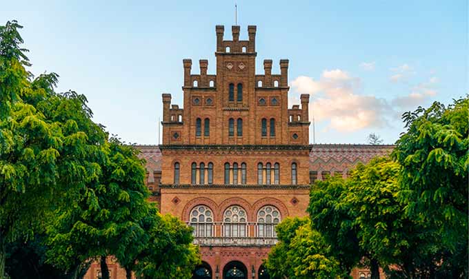 Historic brick building with an ornate, tiered facade and arched windows, framed by green trees.