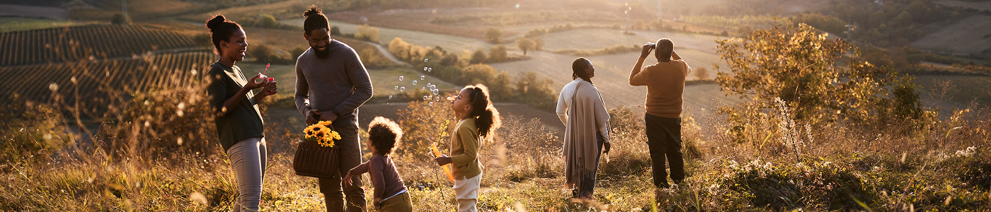 A group of people outdoors in a sunlit vineyard, gathering flowers, blowing bubbles and looking across the countryside.