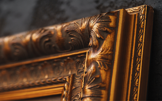Close-up of an ornate gold picture frame featuring carved floral and scrollwork details.