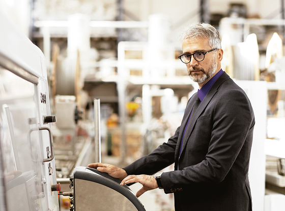 A man in a suit and tie operating industrial machinery in a factory.