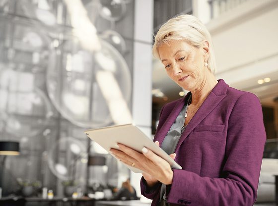 A woman wearing a purple blazer holding a tablet in a modern office setting.