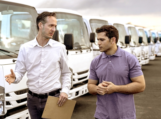 Two men having a conversation in front of a row of white trucks parked outdoors.