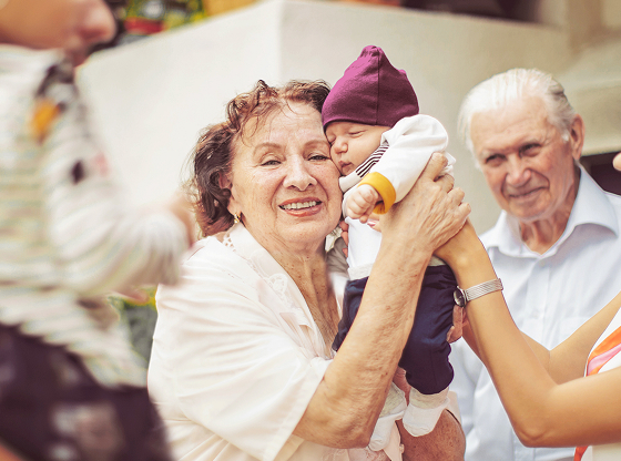 A grandmother, grandfather, and mother gather around a newborn baby.