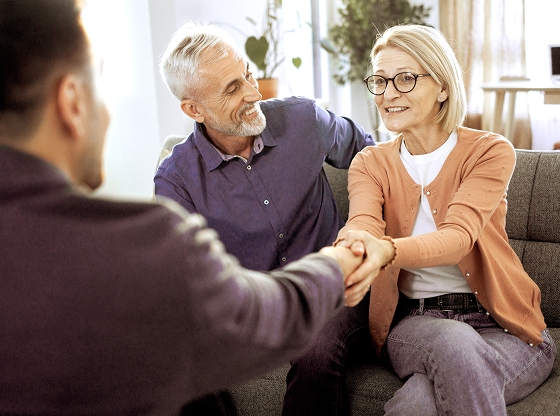 A couple seated on a couch shakes an advisor’s hand