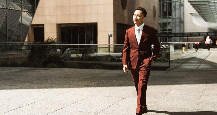 A man wearing a suit walking outdoors near modern buildings.