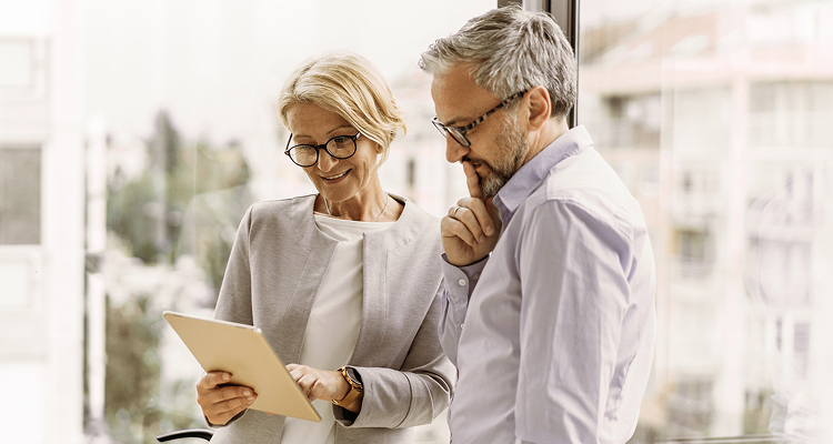Two business professionals standing indoors, reviewing information on a tablet.