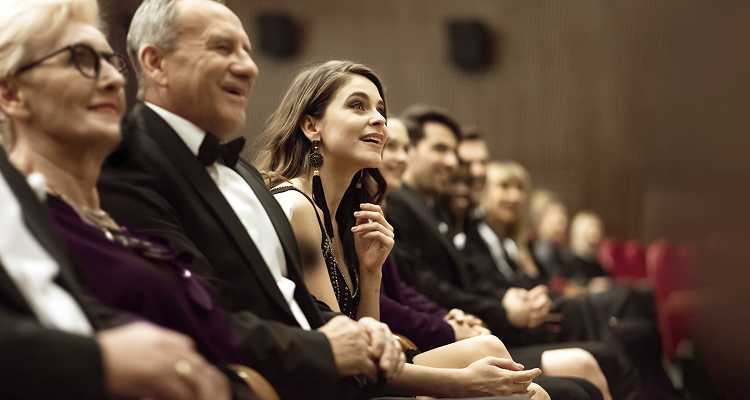 An audience seated in a theater, dressed in formal attire.