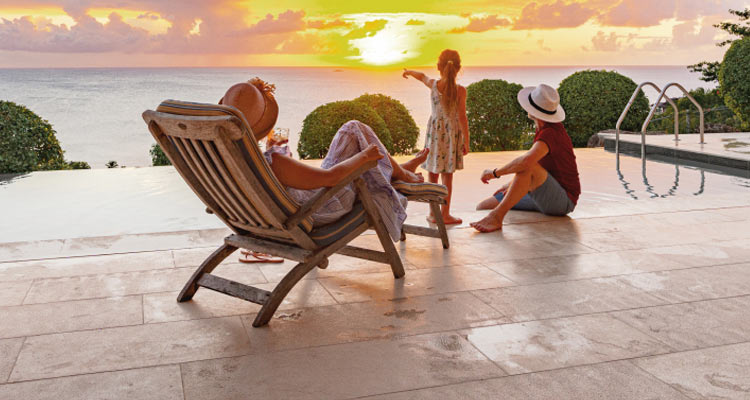 Family lounging by pool overlooking ocean at sunset