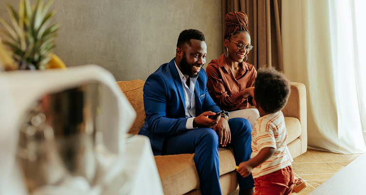 Two adults sitting on a couch near their young child.