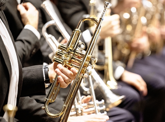 Musicians playing brass instruments, focusing on a trumpet held by a person in formal attire