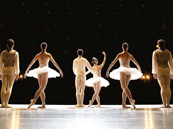Eight ballet dancers pose in a line on stage.