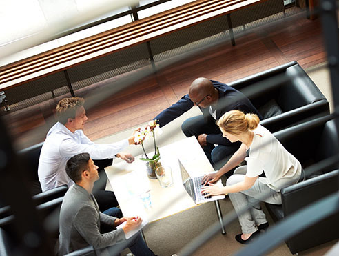 Business professionals seated at a conference table reviewing documents in a modern office with large windows overlooking a city