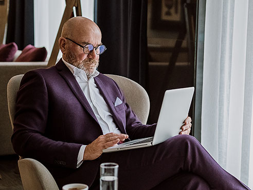 Individual seated in a lounge chair using a laptop in a home or hotel interior setting with a side table and beverages