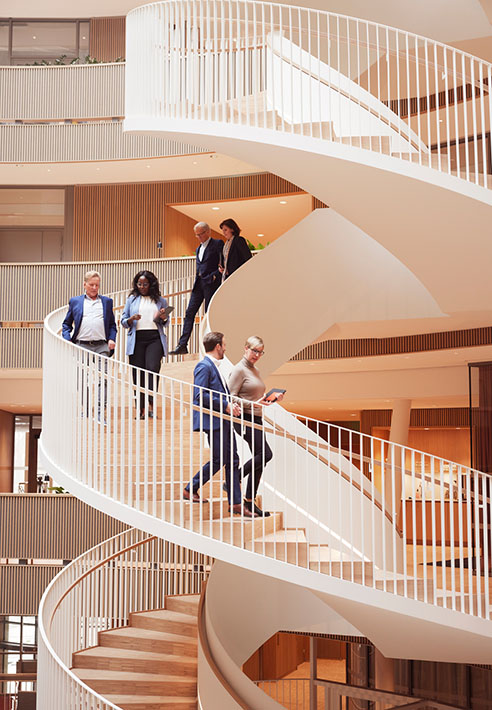 Business professionals walking down a curved staircase in a modern office building with multiple levels