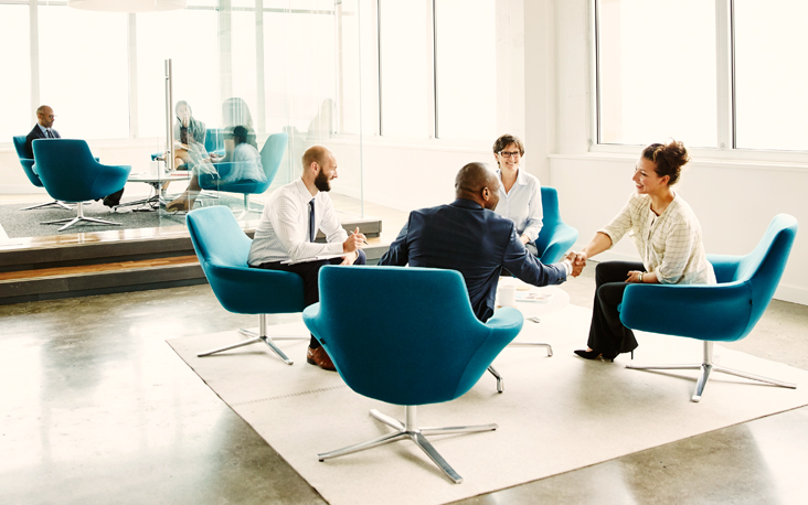 A group of people sitting and smiling at a meeting and two people shacking hands.