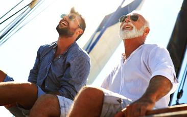 Father and his adult son sittings and smiling with their sunglasses on.